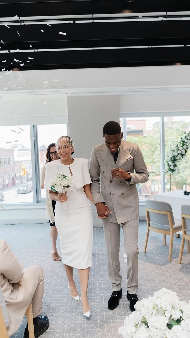 Couple walking hand-in-hand, woman in a chic white midi wedding dress holding flowers.