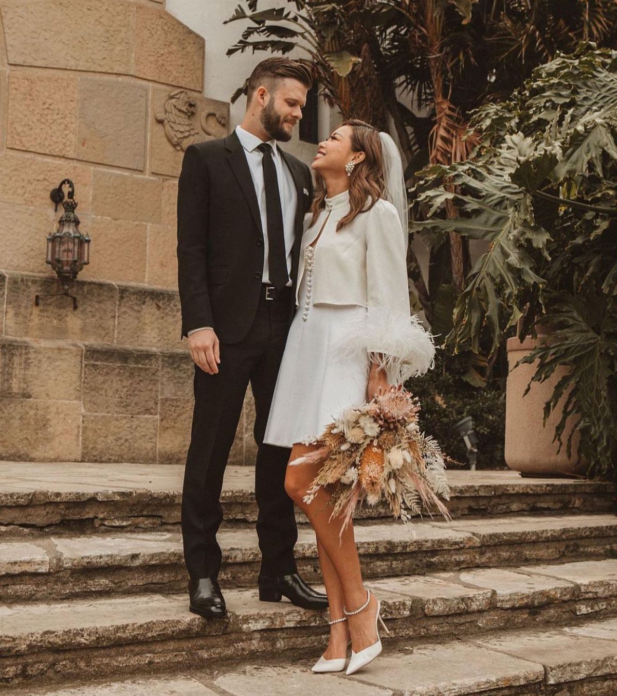 Bride in a short white dress and cropped jacket posing with groom.
