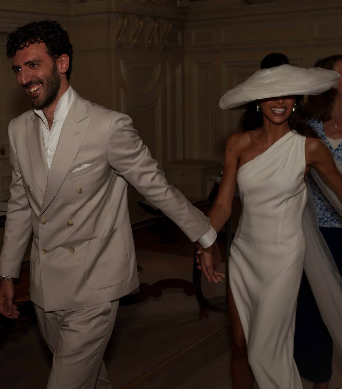 Couple in white wedding attire holding hands in a formal indoor setting