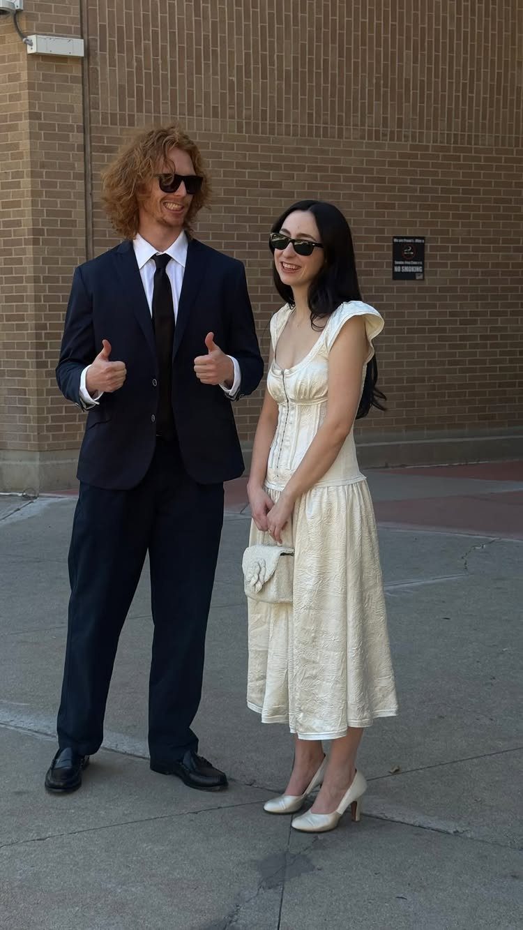 Couple in wedding attire standing outdoors, woman wearing a chic cream midi dress.