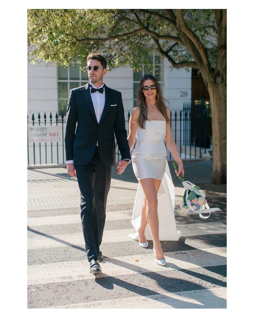 Couple in wedding attire walking across a city street with a short dress train