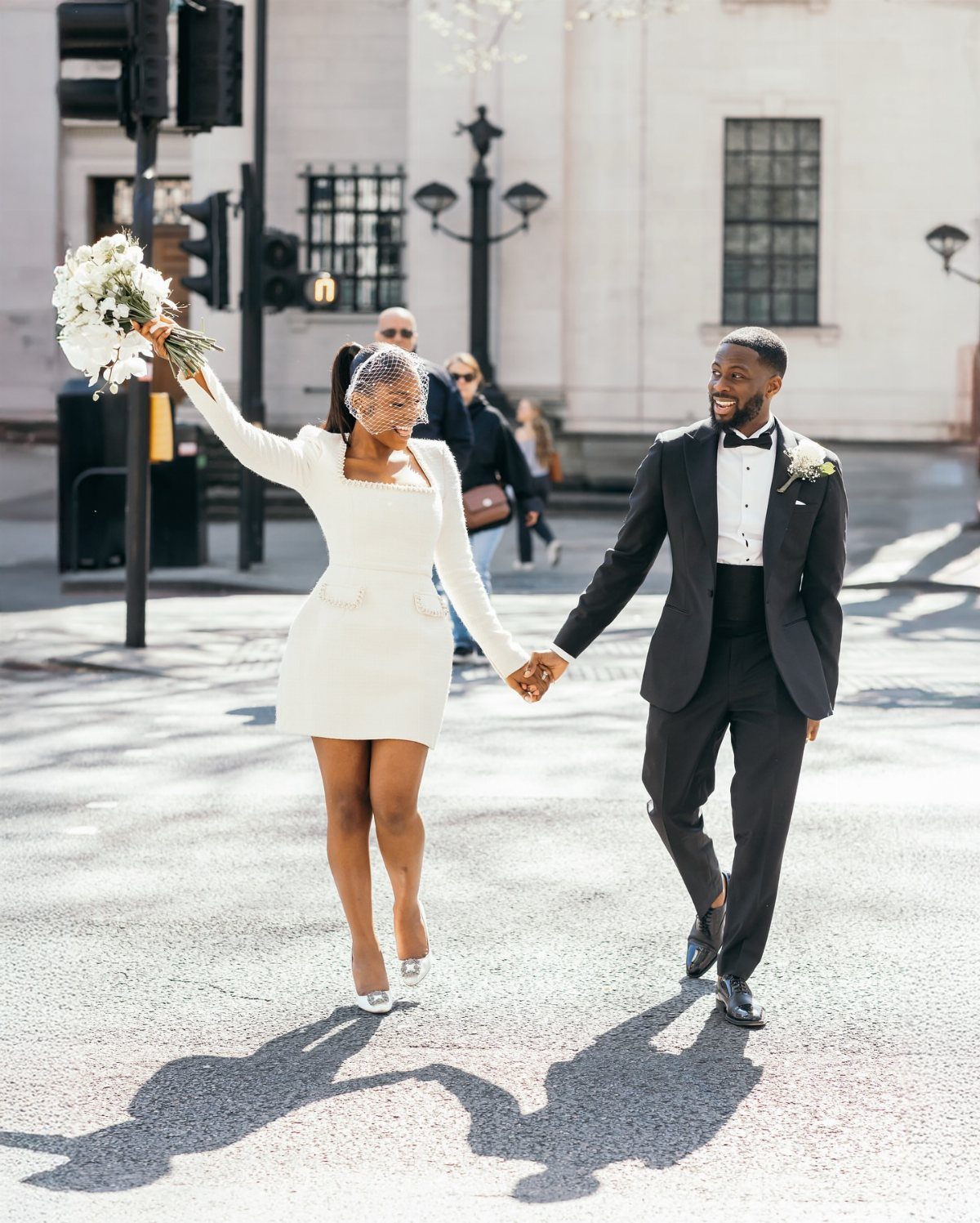 Couple walking in city, woman wearing a short white long-sleeved wedding dress