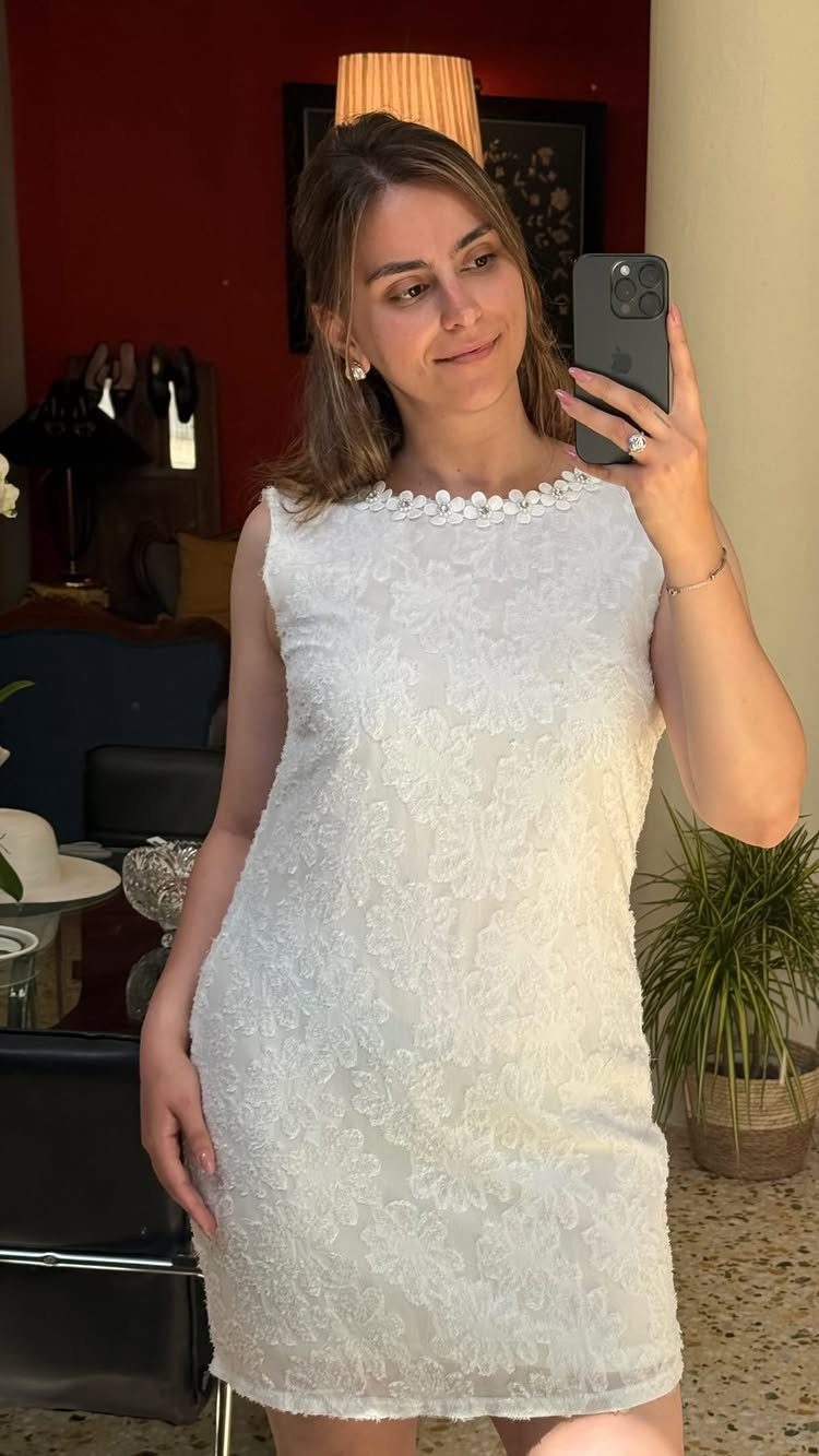 Woman in a white lace mini dress taking a mirror selfie indoors.