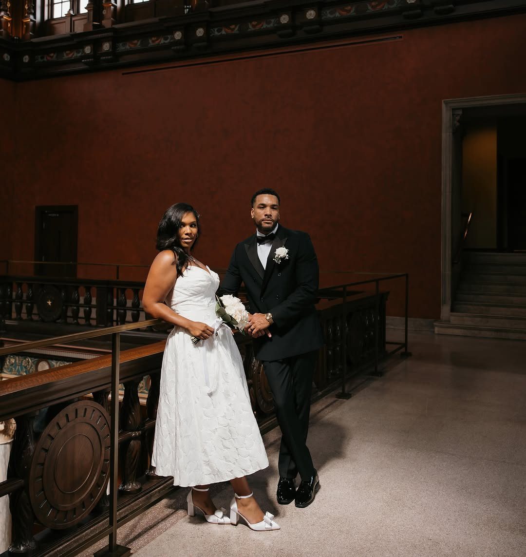 Couple in wedding attire posing in a grand hall with red walls