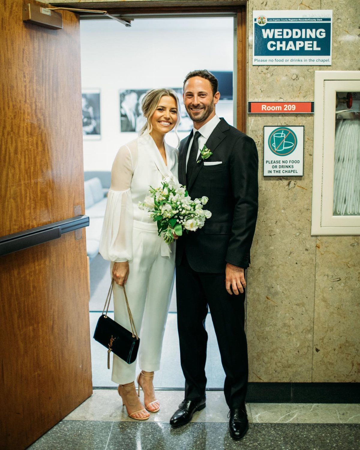 Couple posing in wedding attire in front of a wedding chapel sign.