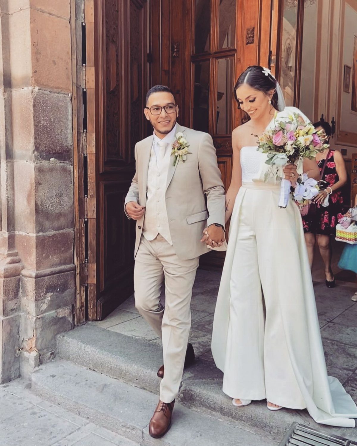Couple walking from a building, woman wearing a white strapless bridal jumpsuit
