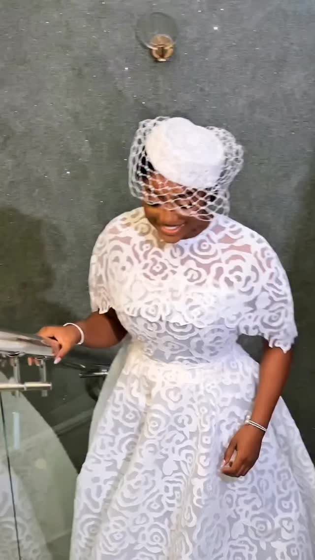 Woman in a white lace wedding dress and pillbox hat with a veil.