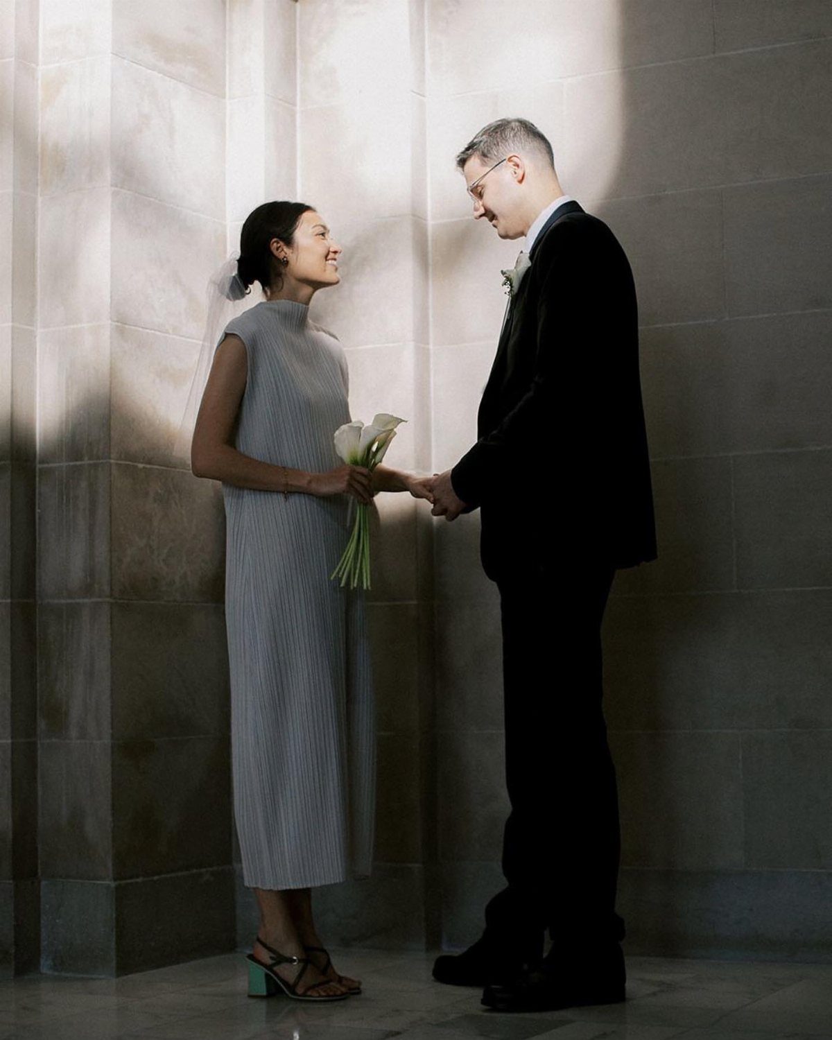 Couple in wedding attire holding hands in a stone hallway with white lilies