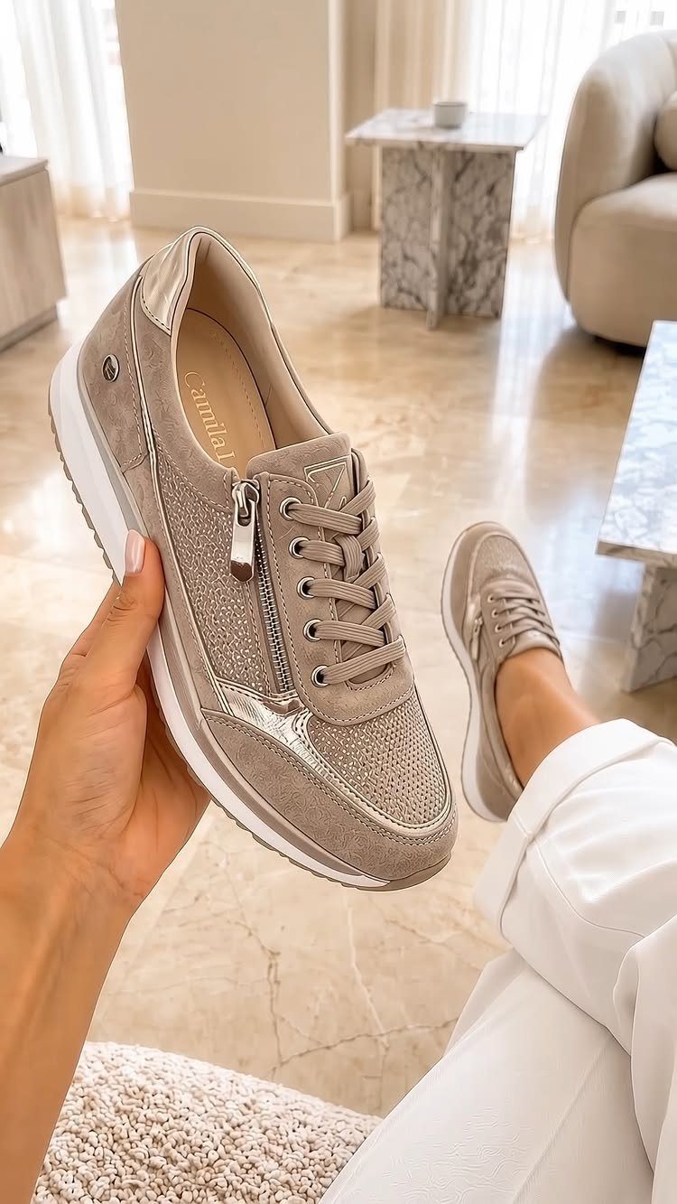 Beige and gold glittery sneakers held by a person in white pants.