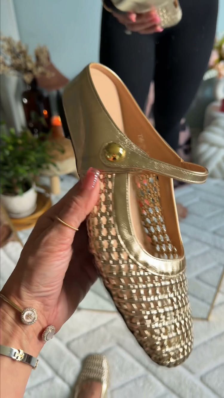 Gold metallic woven flat slingback shoe held by a hand against a home background