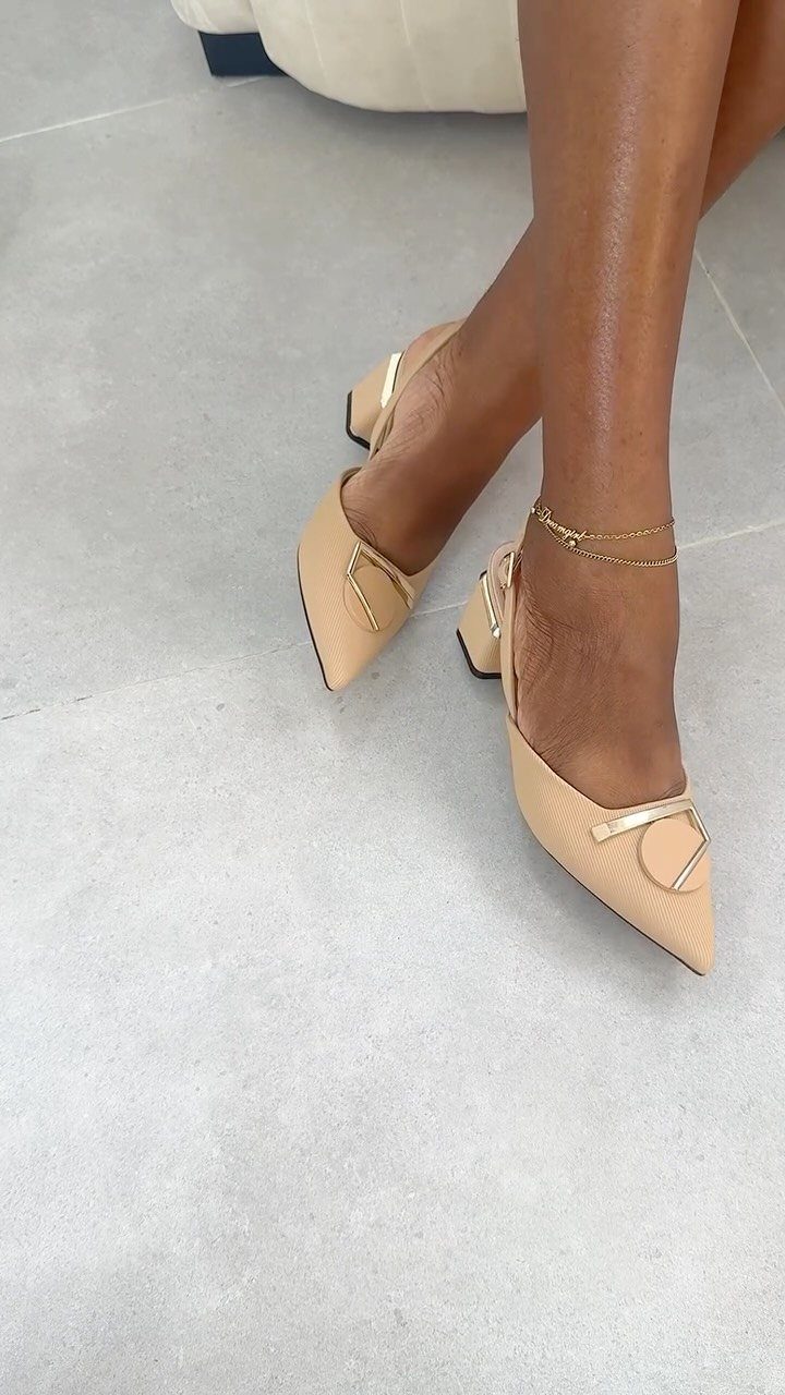 Beige pointed-toe kitten heels with gold accents worn by a person on concrete.