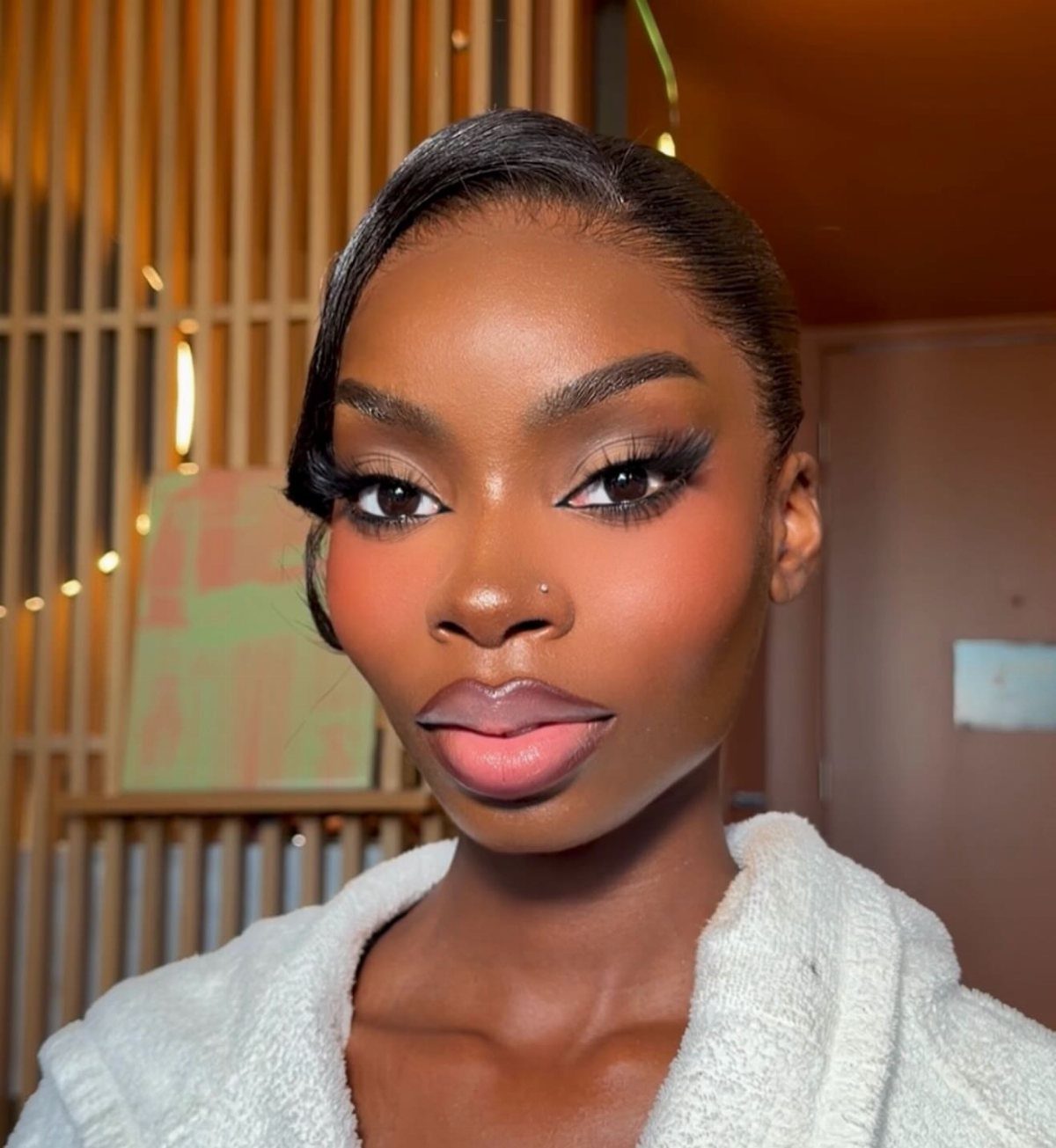 Woman with dark skin wearing glamorous bridal makeup and a white textured robe.