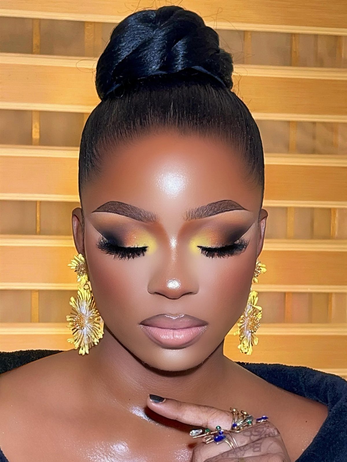 Woman with dark skin wearing luminous golden bridal makeup and gold floral earrings.