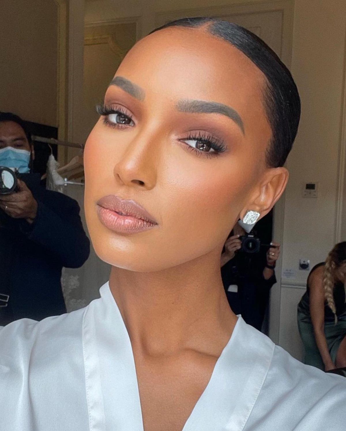 Woman with dark skin wearing monochromatic bronze bridal makeup and a white robe.