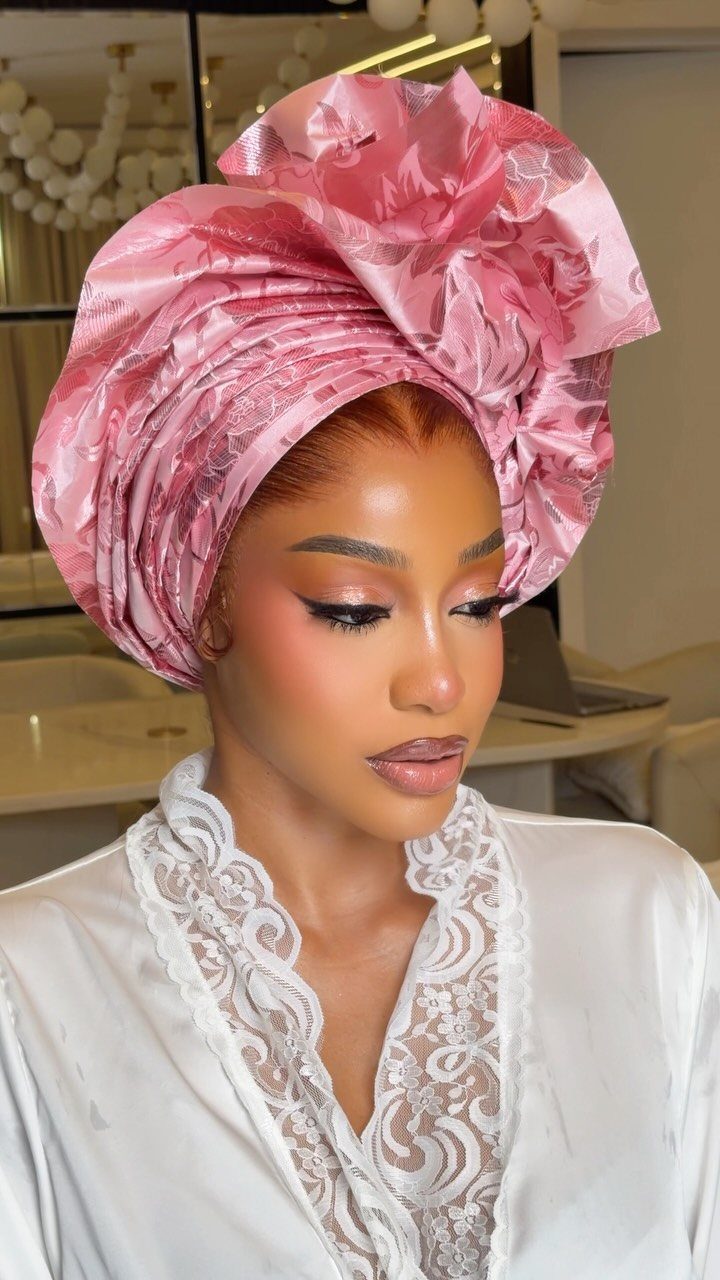 Woman with dark skin wearing a pink headwrap and bridal makeup with glowing skin.