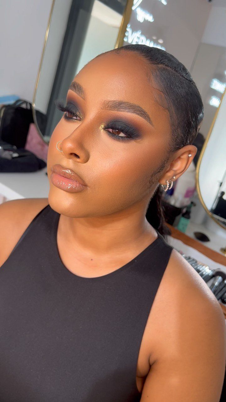 Woman with dark skin wearing dramatic smoky eye makeup and glossy nude lips.