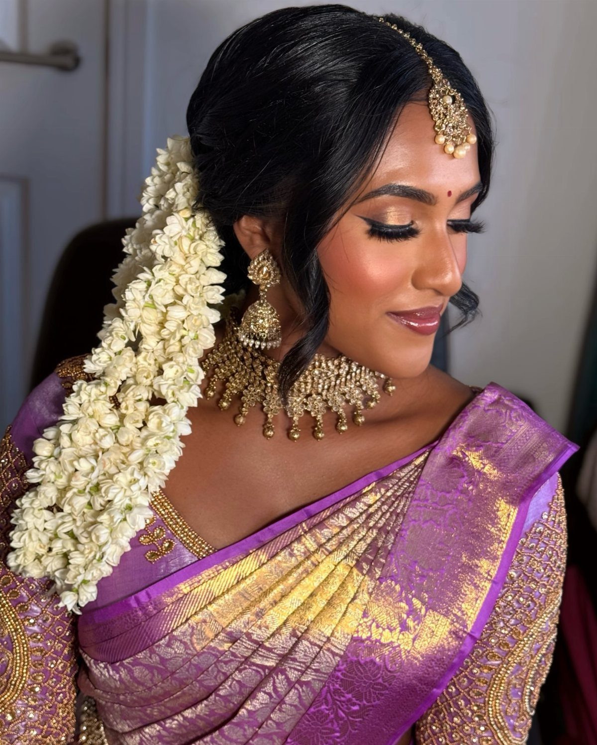 Woman in purple saree with gold bridal makeup and white floral hair garland