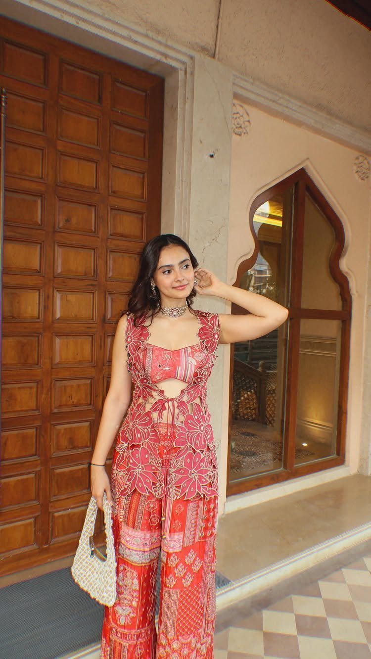 Woman in red and gold patterned co-ord set posing by a wooden door.
