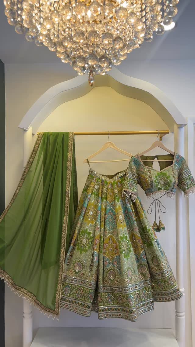 Green and gold embroidered lehenga choli with dupatta hanging under a crystal chandelier.