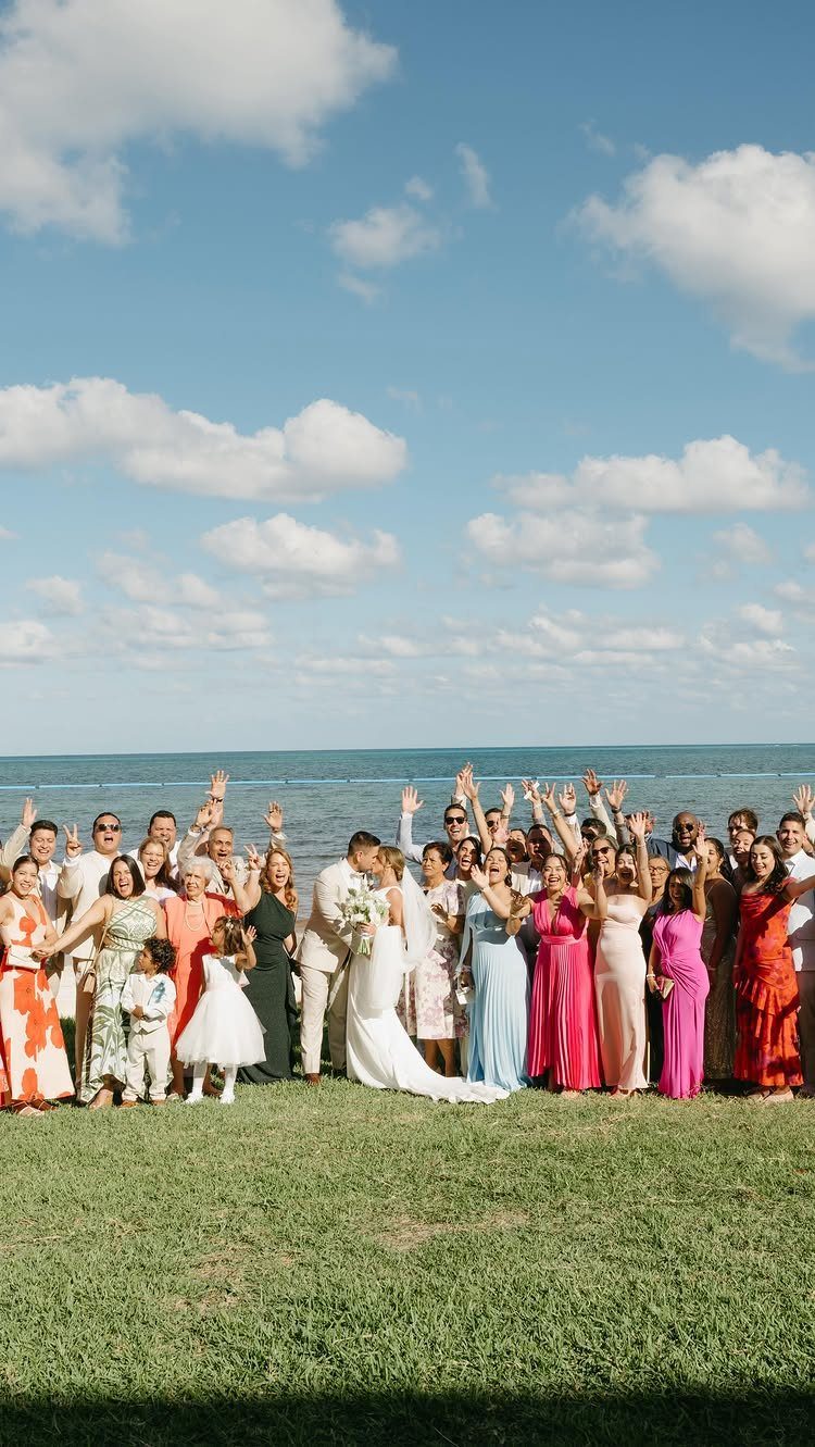Wedding guests in colorful summer dresses standing on grass by the ocean beach.