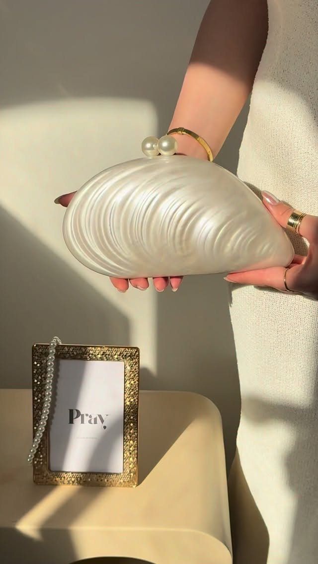 White shell-shaped clutch bag with pearl details held by a person in white.