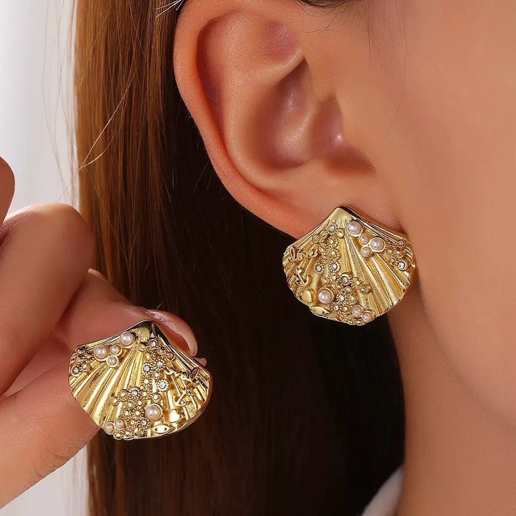 Gold shell-shaped earrings with pearls worn on an ear and held by hand.