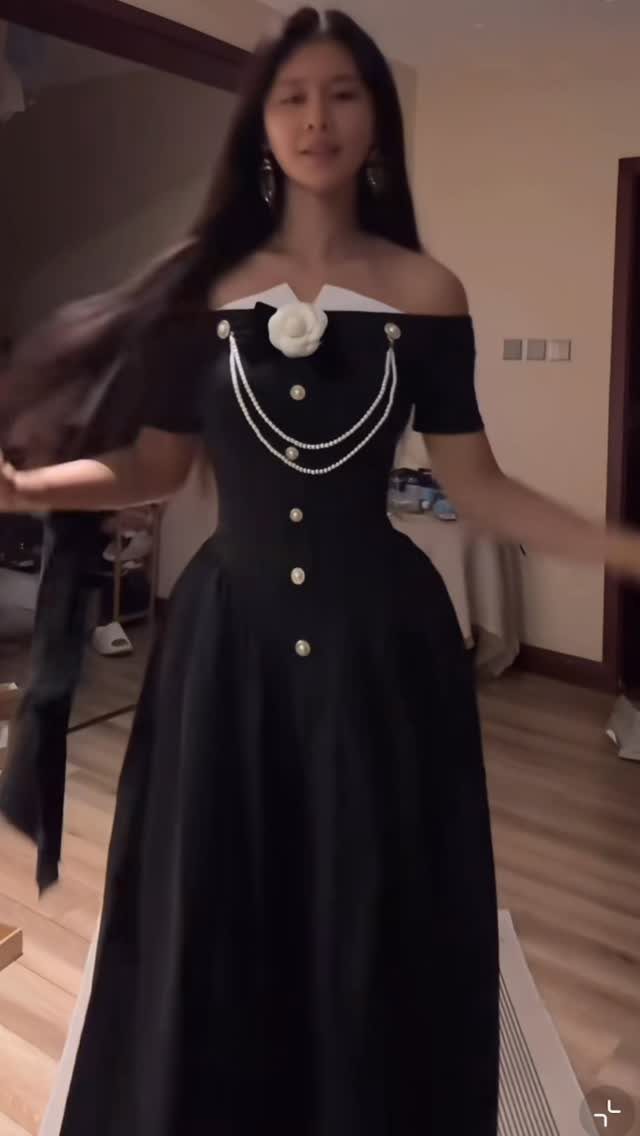 Woman wearing a black floor-length dress with white collar and pearl accents.