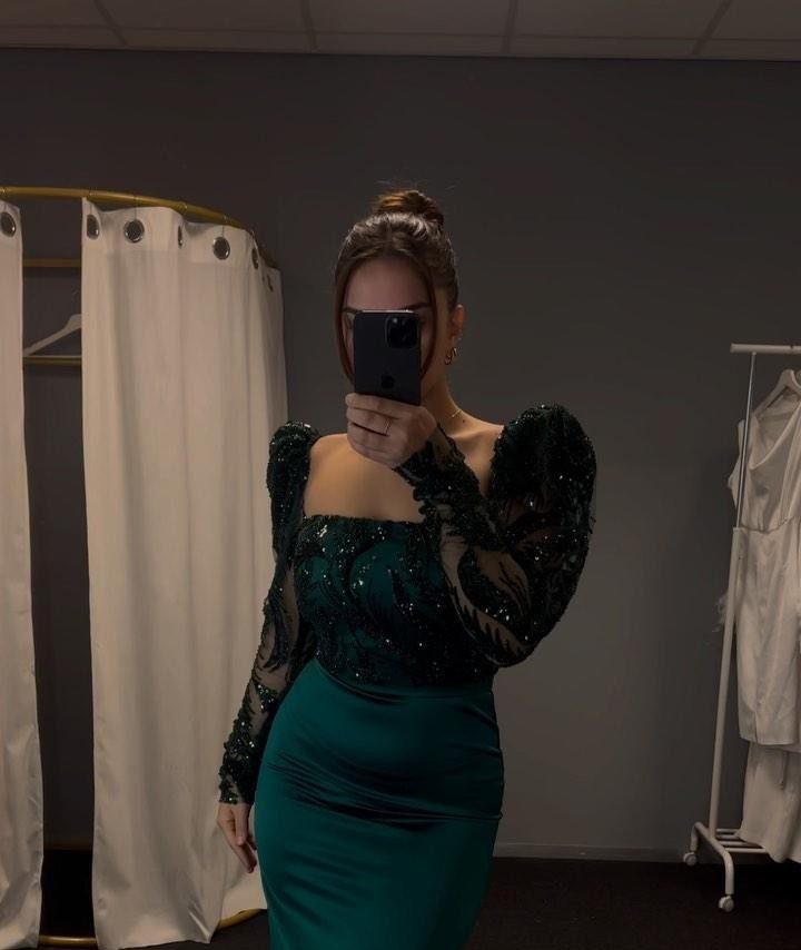 Woman in a dark green sequined and satin dress taking a mirror selfie.