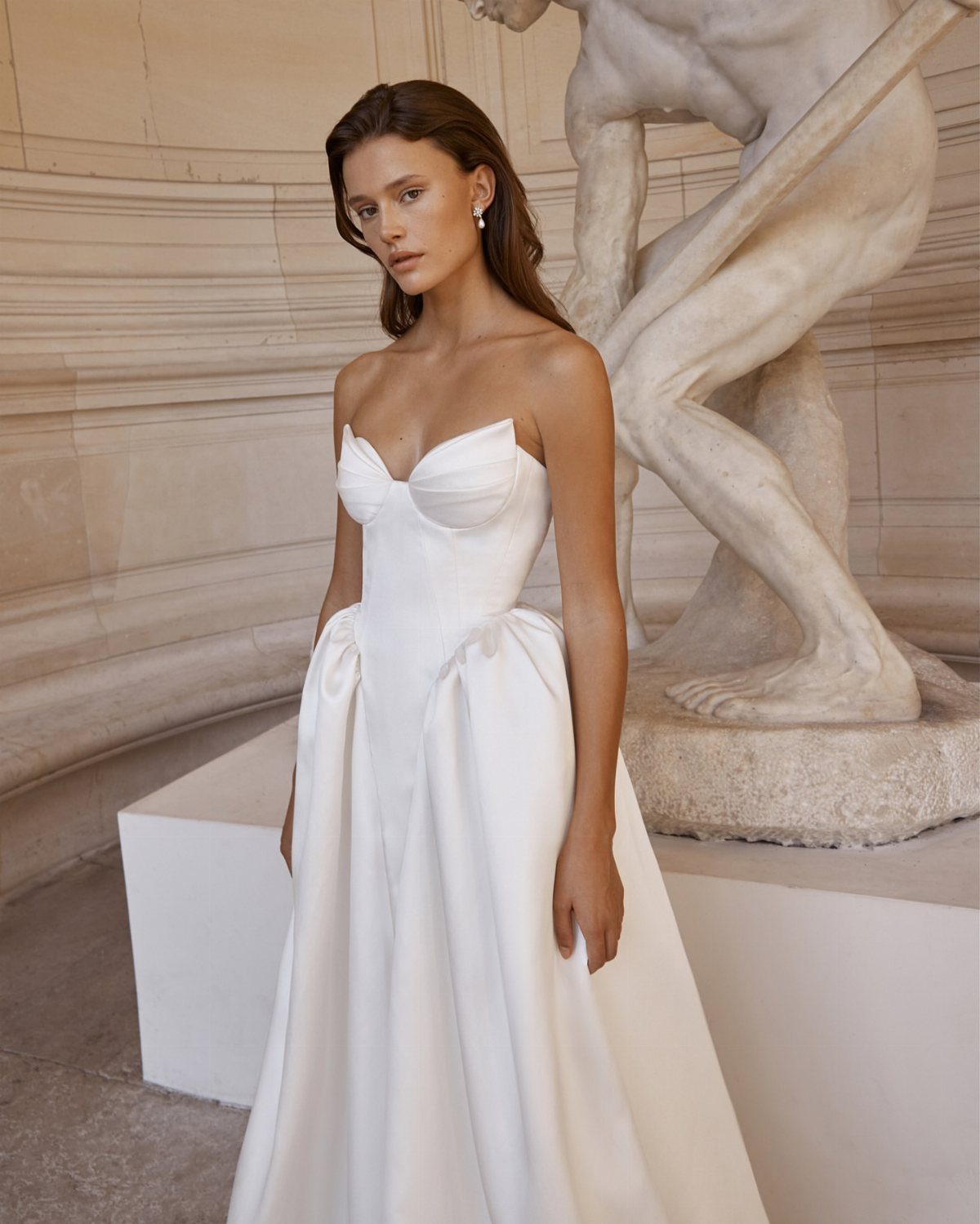 Woman in a strapless white satin drop waist wedding dress posing by a sculpture