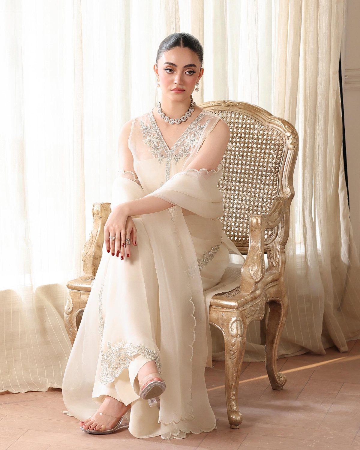 Woman in a cream flowy wedding dress with silver embroidery sitting in gold chair