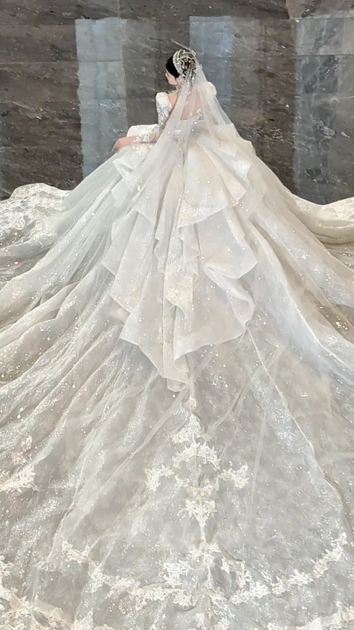 Layered white wedding dress with a long train and lace embroidery on marble floor