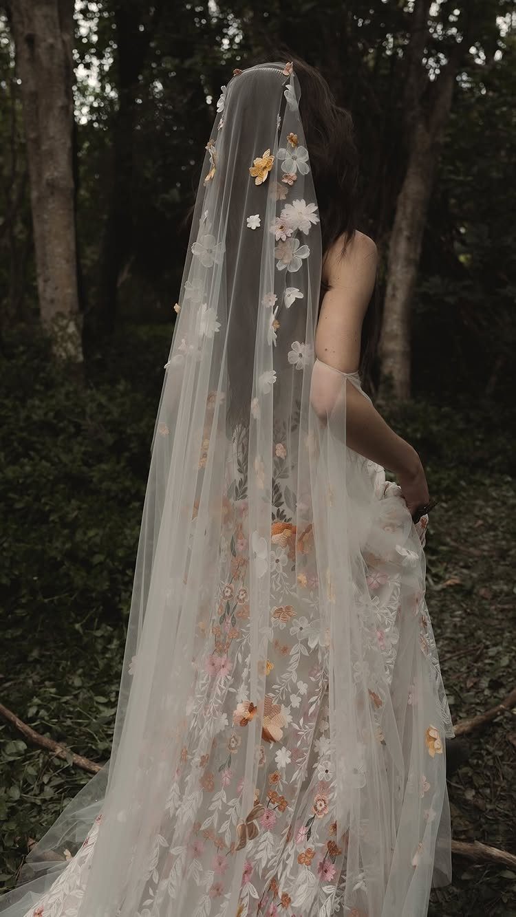 Woman in a floral wedding dress and veil standing in a dark forest