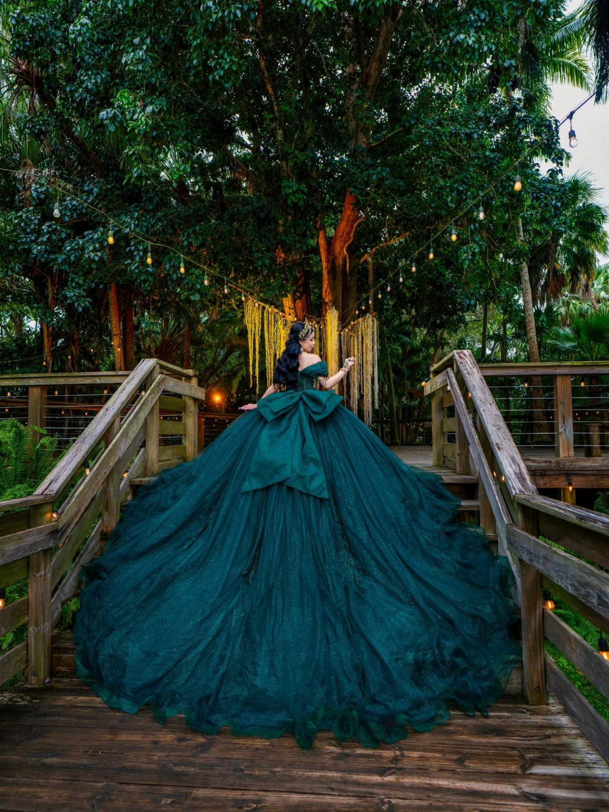 Woman in a voluminous dark teal tulle ball gown on a wooden forest bridge.