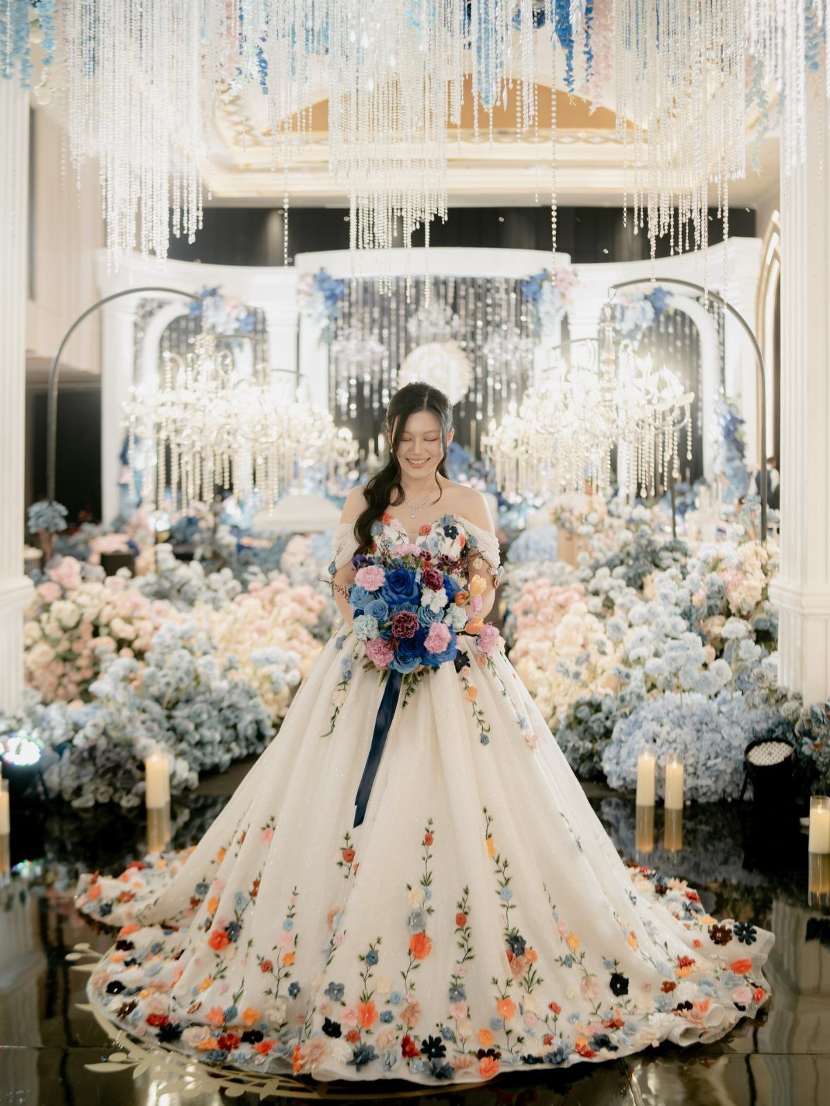 Woman in an off-the-shoulder white wedding gown with floral embroidery holding a bouquet.