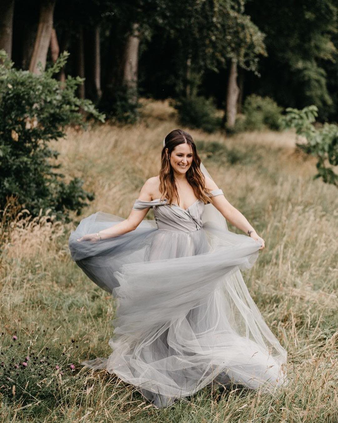 Woman in a flowing grey tulle off-the-shoulder gown posing in a grassy field
