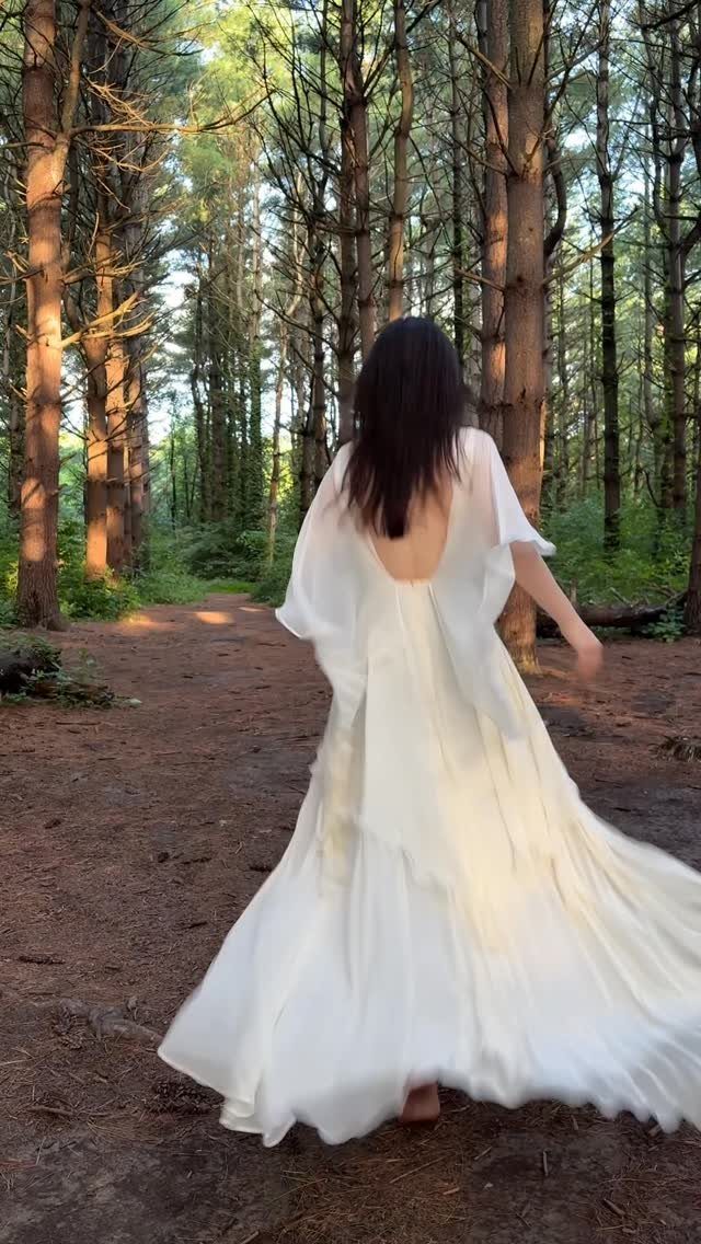 Woman in a flowing white wedding dress walking through a sunlit pine forest