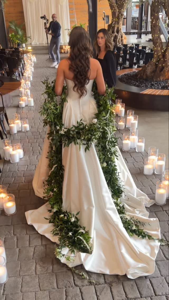 Woman in white wedding dress with green leaf garlands on a candlelit path