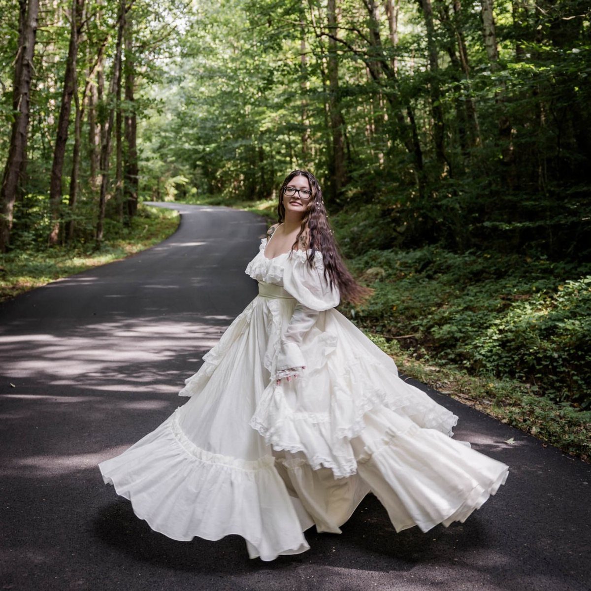 Woman in a voluminous white tiered gown standing on a road in a forest
