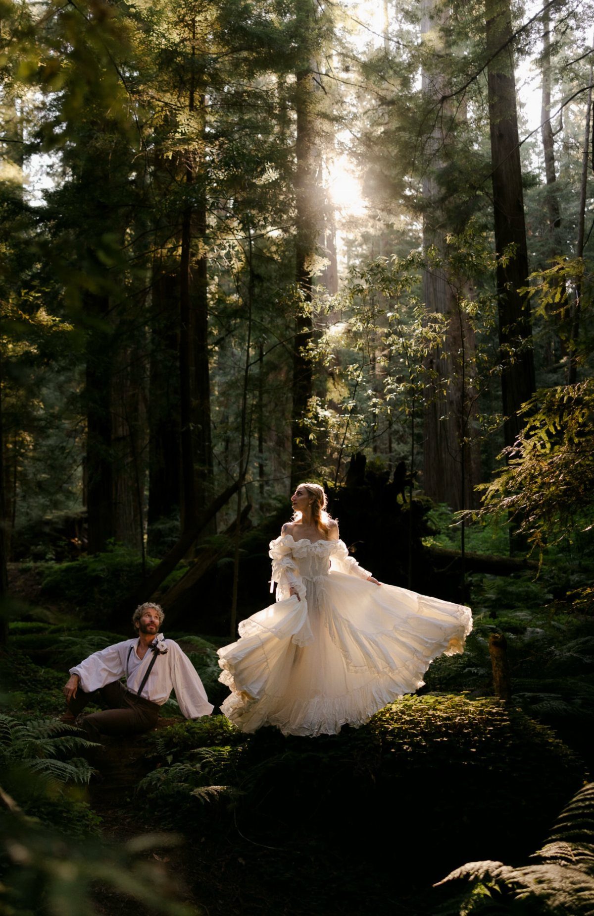Woman in a voluminous white wedding gown standing in a sunlit redwood forest.