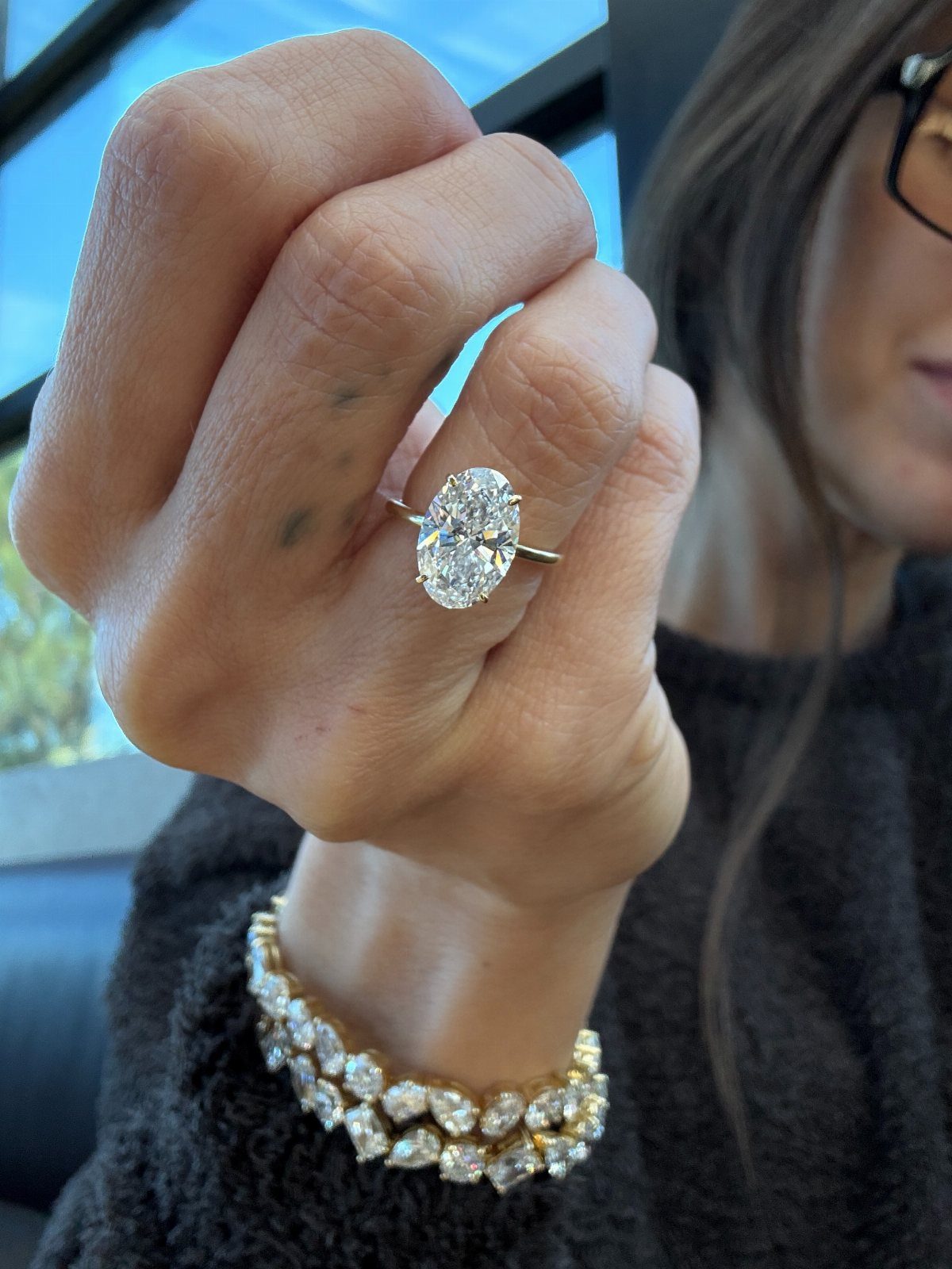 Oval-cut diamond engagement ring and diamond tennis bracelet on a person's hand