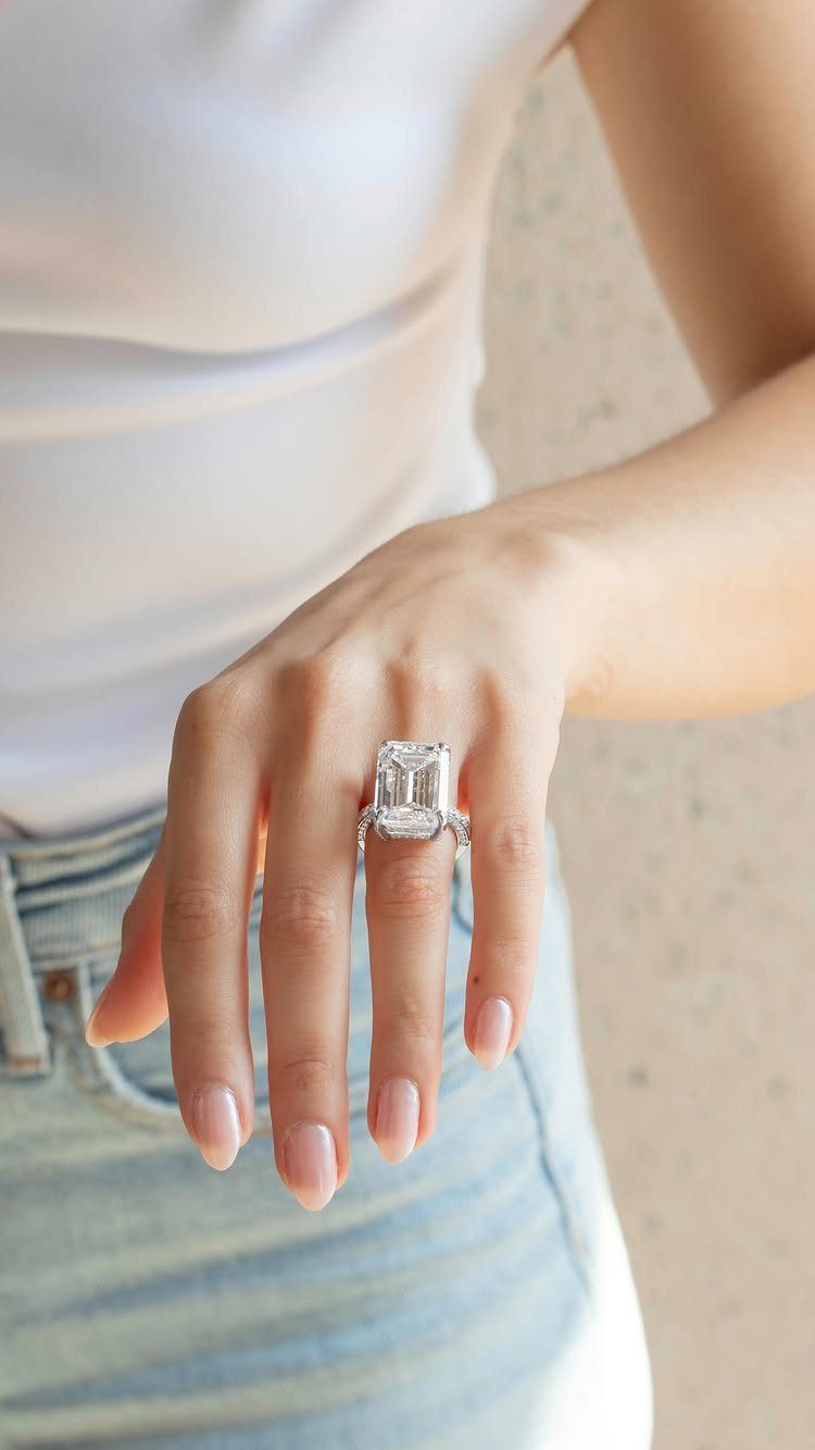 Emerald-cut diamond engagement ring on a woman's finger wearing white and denim.