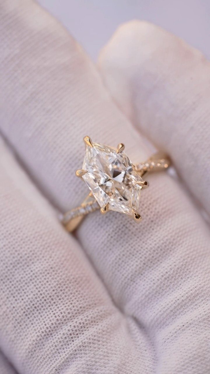 Gold engagement ring with a marquise-cut diamond held by a gloved hand.