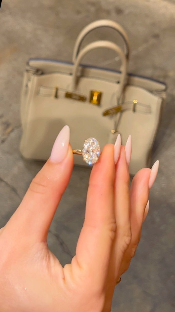 Gold engagement ring with a large oval diamond held by a manicured hand.