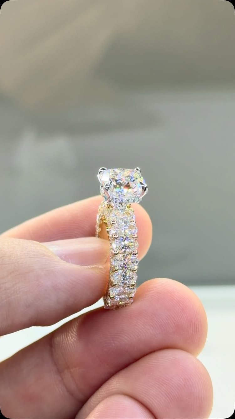 Square-cut diamond engagement ring with a pavé band held between two fingers.