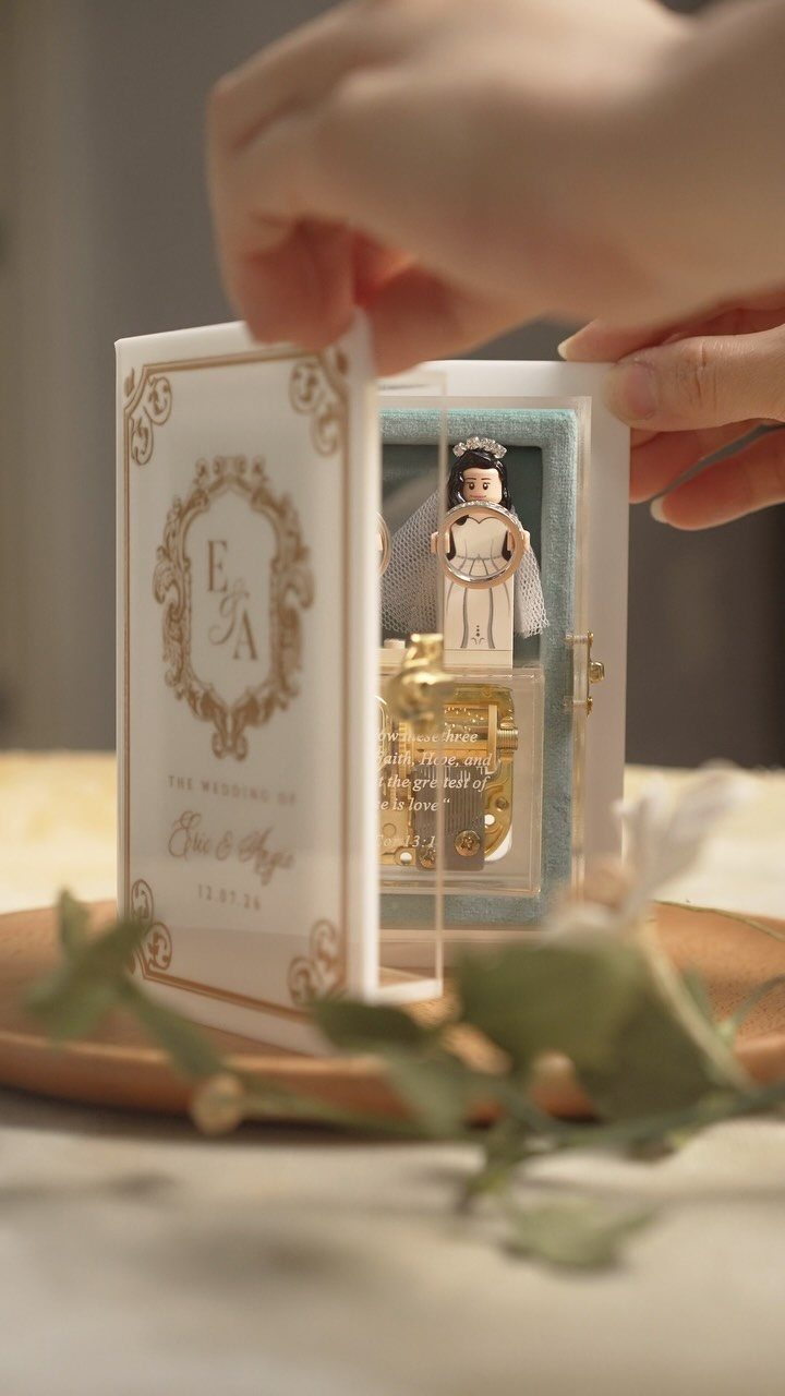 White book-style ring box opening to reveal a bride figurine and gold chest.
