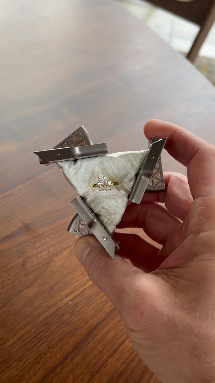 Silver geometric ring box held in a hand containing a diamond engagement ring