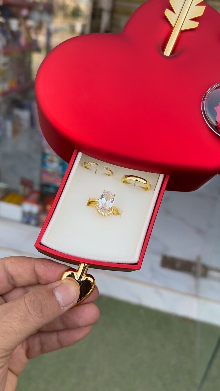 Red heart-shaped ring box holding three gold diamond rings with a gold arrow