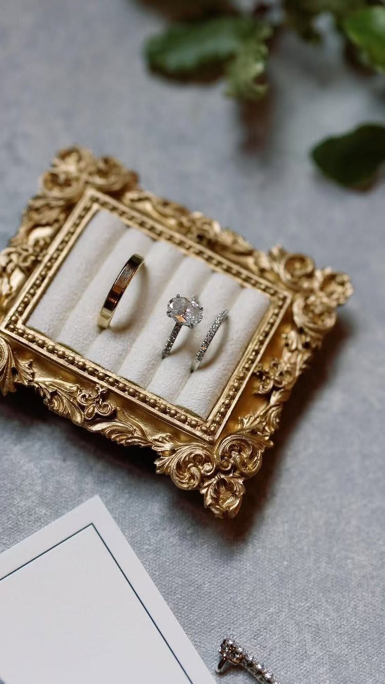 Three diamond and gold rings in an ornate gold frame ring box