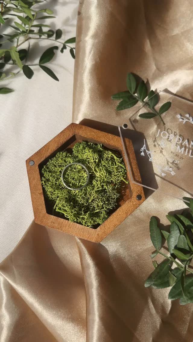 Hexagonal wooden ring box with green moss holding a silver engagement ring