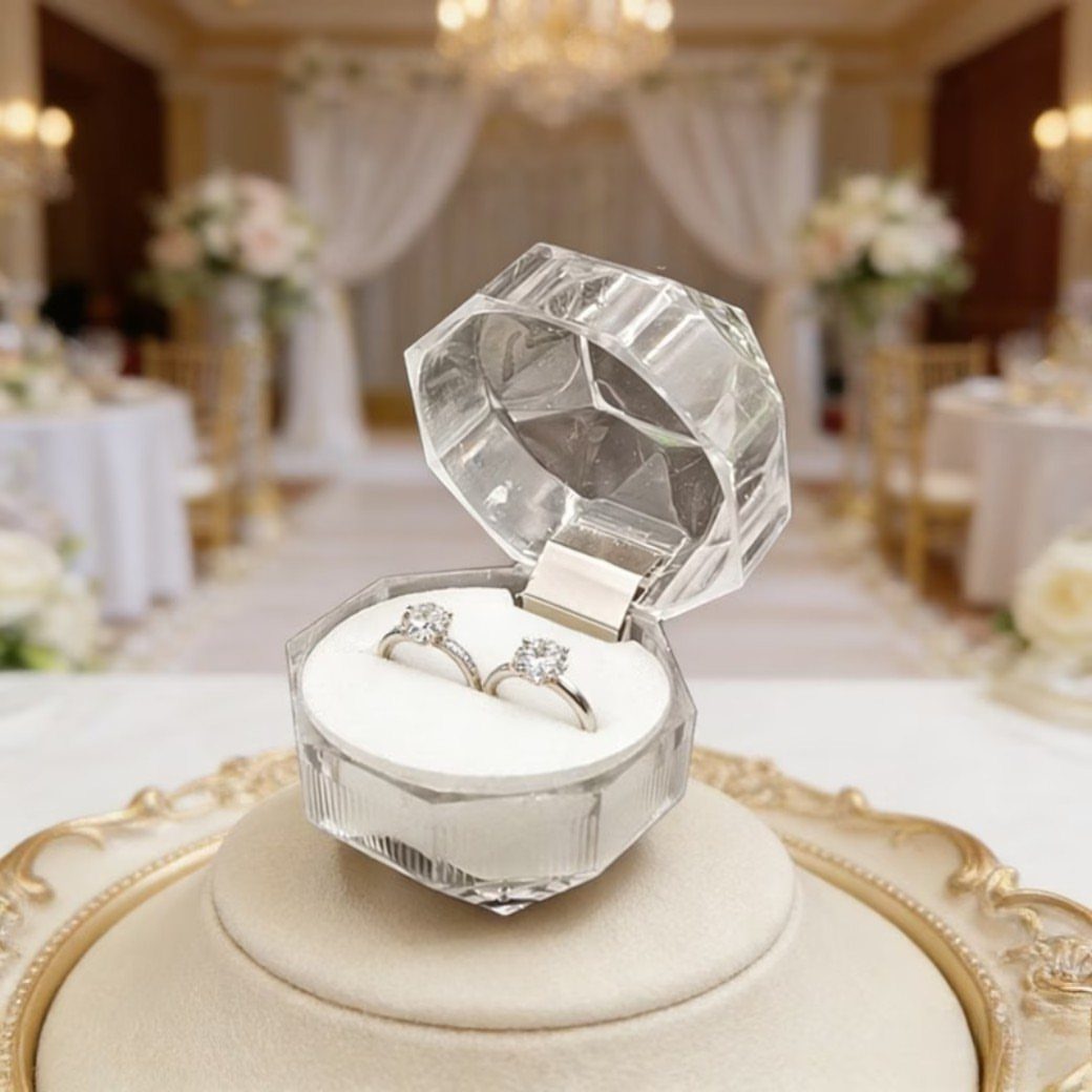 Diamond-shaped transparent acrylic ring box holding two diamond rings in a ballroom